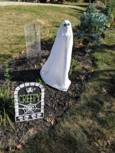 A creepy white lady Halloween decoration with a headstone in front of it that says "creepy."