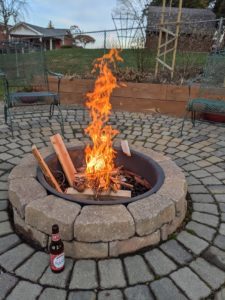 A patio with a fire pit in the middle with a roaring fire, blue sky in the background.