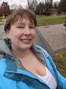 A selfie of me outside, hair is flat, wearing a raincoat, but also showing cleaveage.