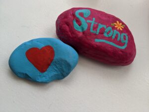 Two painted rocks. One is blue with a heart. The other is pink and says, "Strong."