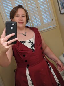 A selfie. I'm wearing a red dress with a white V on the chest with some black details, there are three buttons down each side of the dress.