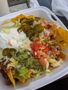 A takeout container of nachos with everything on them.