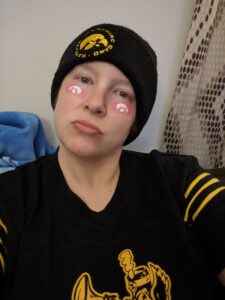 Amanda all decked out in Iowa Hawkeye gear. Black Iowa Hawkeye Marching Band stocking cap, black Iowa shirt, pink Iowa Hawkeyes temporary tattoos under both eyes.