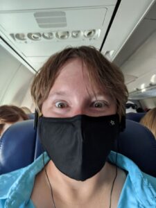 Selfie sitting in a seat on Southwest Airlines. I'm wearing a black mask, my hair is short and a little unruly, and I have on a bright blue shirt.