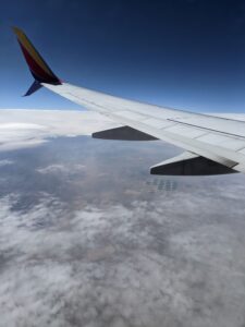 Looking out the airplane window. Part of the wing is visible. There are round circles on the ground in the distance that make a square shape. 