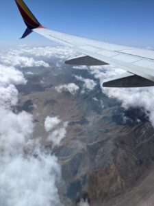 Looking out the airplane window. Part of the wing is visible. Non-snow capped mountains are below. 