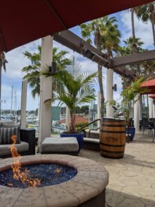 The open air bar at the hotel. No people are present in the picture, but there are posts that are holding up shade overhead and palms and a barrel.