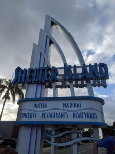 A white sign with blu lettering that says: Shelter Island.