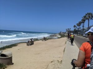 Waling along the beach, but we are on the sidewalk. The waves are rolling in and the sky is perfect blue. There are palm trees on the other side of the road we are walking by. Some Athenas are in front of me.