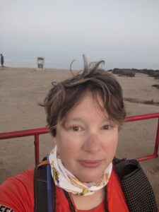 Selfie. It's morning. The Pacific Ocean is behind me and there's a beach in front of that. My hair is kind of flying in the wind and I'm wearing a buff around my neck that says "Project Athena."