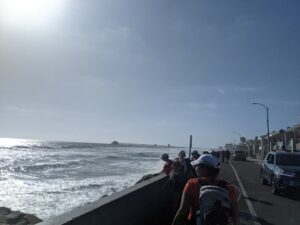 Later in the day, the sun to the west. The Pacific Ocean to the left. Athenas in front of me as we walk on a sidewalk overlooking the shoreline.