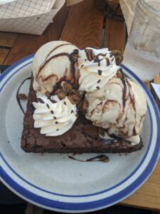 A giant chocolate brownie with ice cream and whipped cream on top of it.