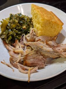 A plate with collard greens, cornbread, and meat - pork or chicken.