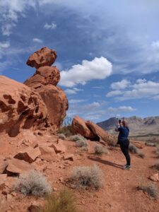 Amanda taking picture of a rock formation. Blue sky with clouds.