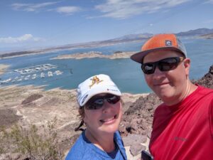 Amanda and Gabe in front of Lake Mead. We are both wearing ballcaps. Amanda's is white/Athena hat. Gabe's is orange. Amanda is in blue, Gabe is in red. We clash. 