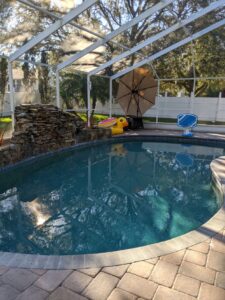 A backyard pool with a pool cage over it. There's a fountain, but it's shut down for the winter. It's rocks on the side. There's a giant inflatable duck next to the pool.