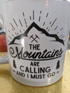 A coffee mug that has a mountain on it and says: The Mountains are calling and I must go.