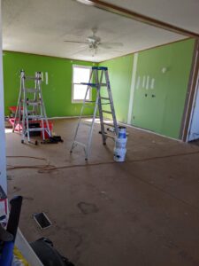 Inside of my sister's house. A room with only subfloor, green walls. A ladder in the middle. Construction zone, but also a clean slate.