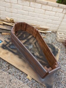 An open wooden coffin. The lid wasn't finished yet. It's in the backyard on some cardboard having been spray painted brown with some black as well.