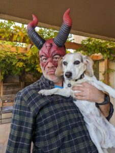 Gabe holding Edie beagle. She's just a beagle, but he's wearing a half mask that's a red devil with horns. Not pictured: Arthur who did not like the mask At All.