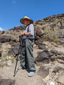 My dad dressed up for a hike with a pole and a hat on, suspenders and comfy pants. We are at Petroglyph National Monument.