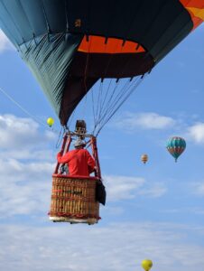 A balloon up in the air. A guy in a red shirt is in it, looking away from us. Ther are others in the distance, but it feels like we're going up with him here!