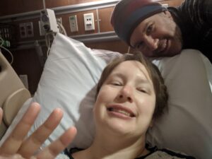 Selfie, I'm in a hospital bed, Gabe is behind me. We're both smiling, i look high.