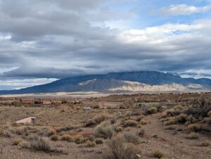 Sandia Mountain in the distance. Sun is hitting the base, but the top is shrouded in clouds. The desert stretches out before us, but you can still see blue sky.